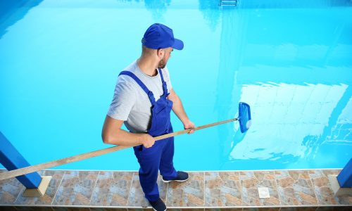 Male worker cleaning outdoor pool with scoop net